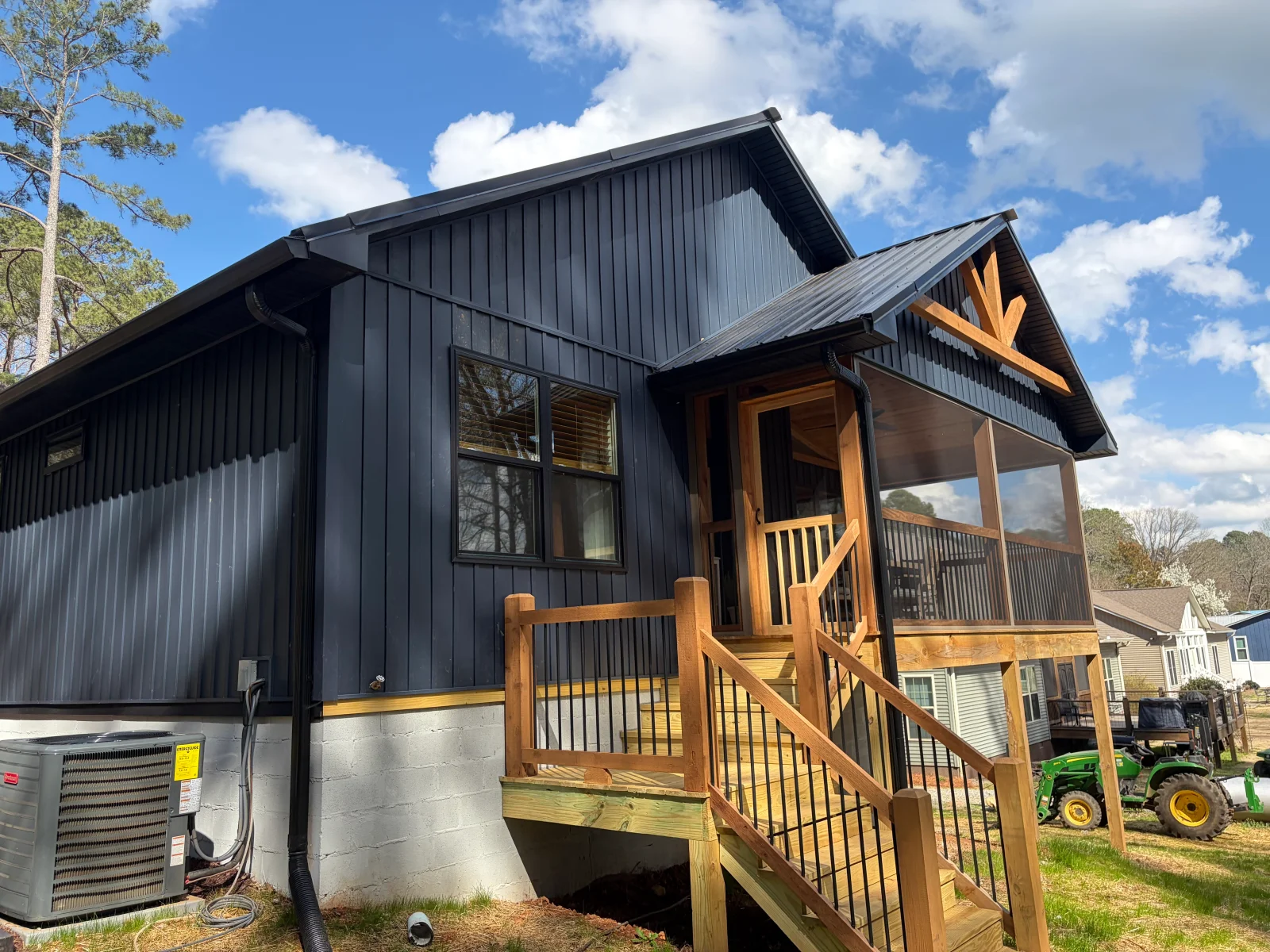 Black corrugated metal home with wood porch, railings, and gable trim