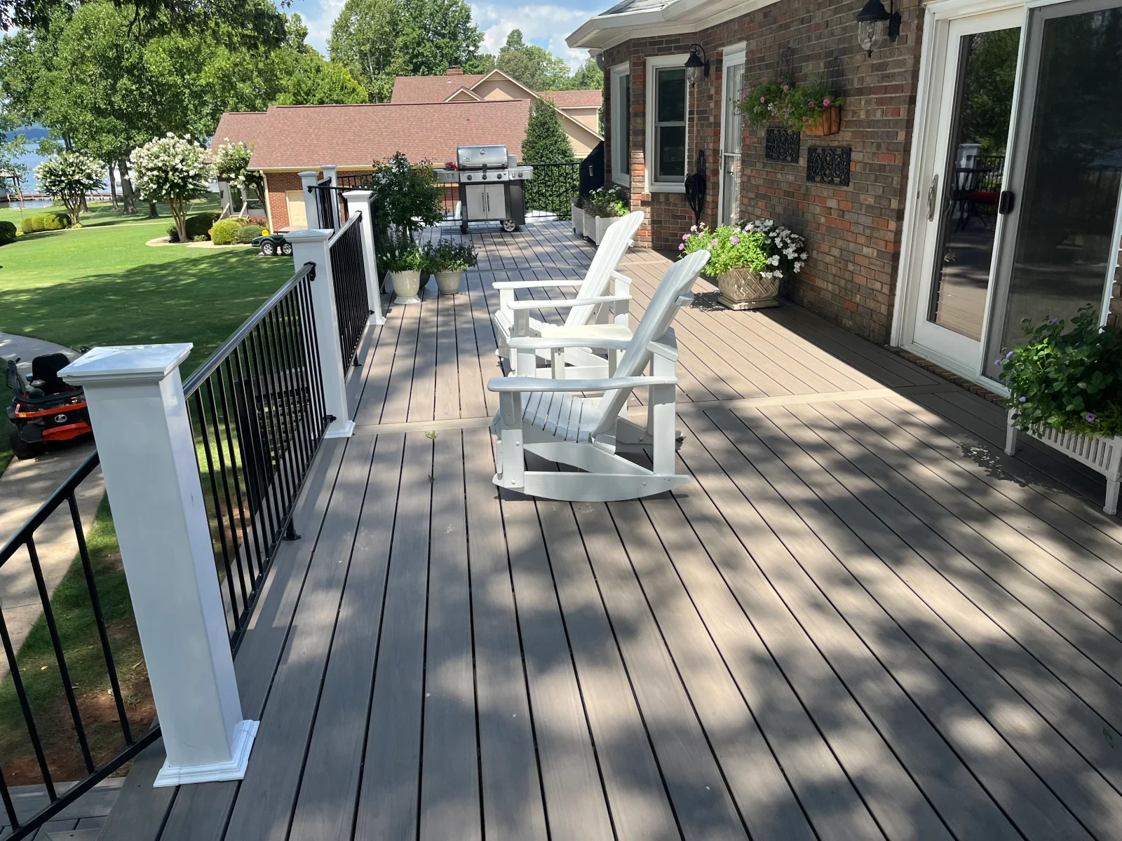 Gray composite deck with white railing, built-in planters, and white Adirondack chairs overlooking lawn