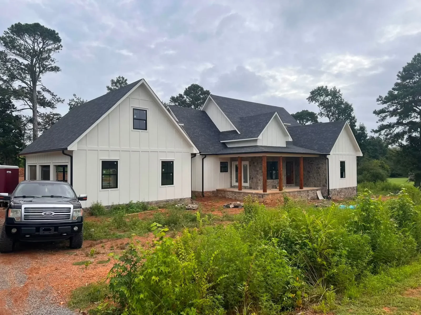 White board-and-batten farmhouse with stone veneer, gabled rooflines, and covered porch under construction