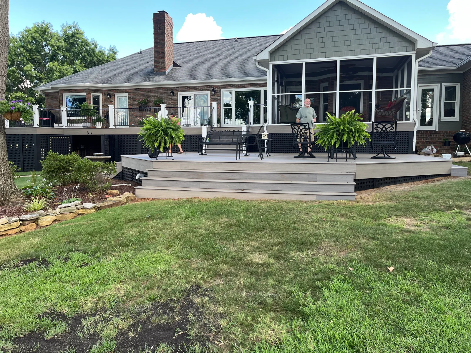 Gray composite deck with black lattice skirting, screened porch addition, and brick home exterior
