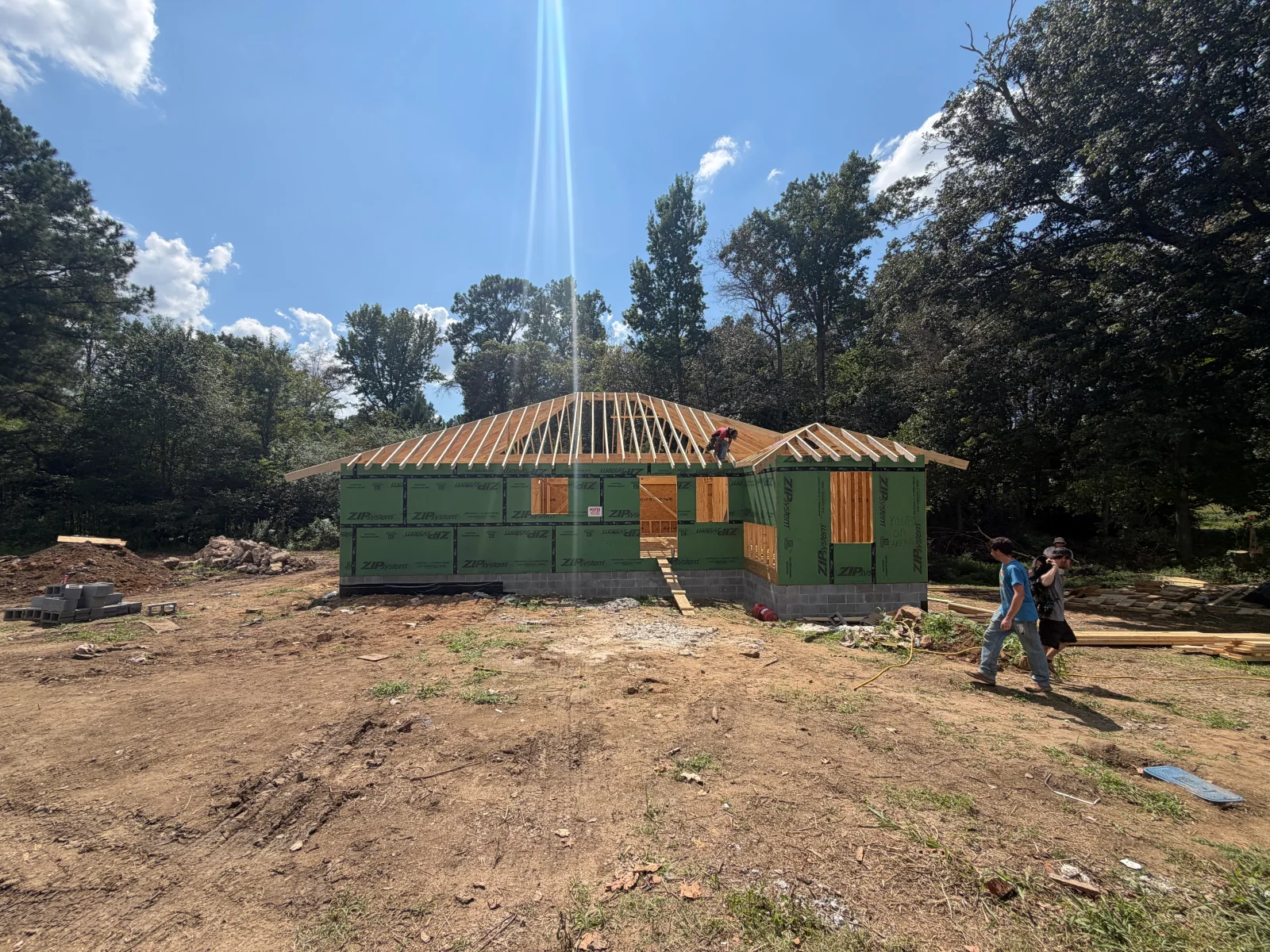 Custom home framing with wooden roof trusses, green house wrap, and installed door and window frames during construction