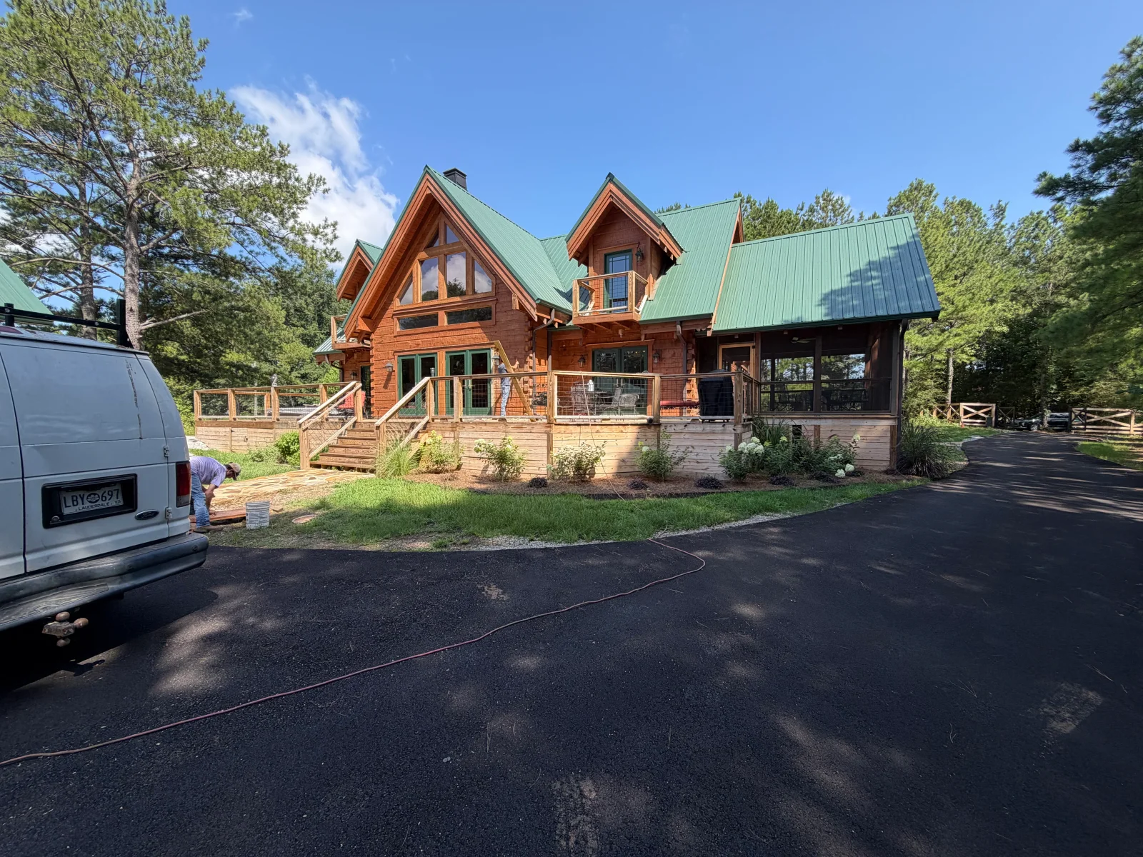 Custom log home with green metal roof, timber siding, and wraparound deck with cable railings