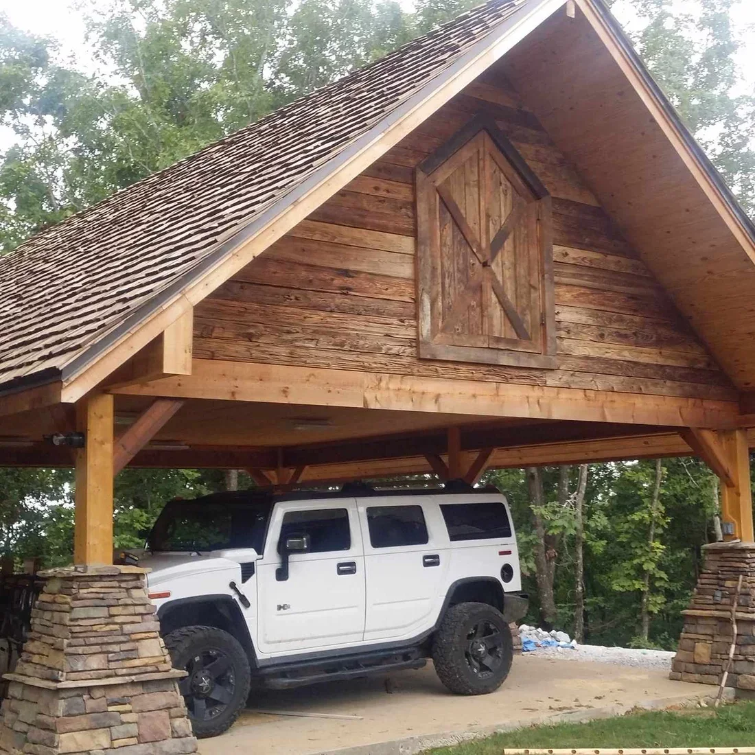 Timber frame carport with exposed beams, wood shingle roof, and stone pillars