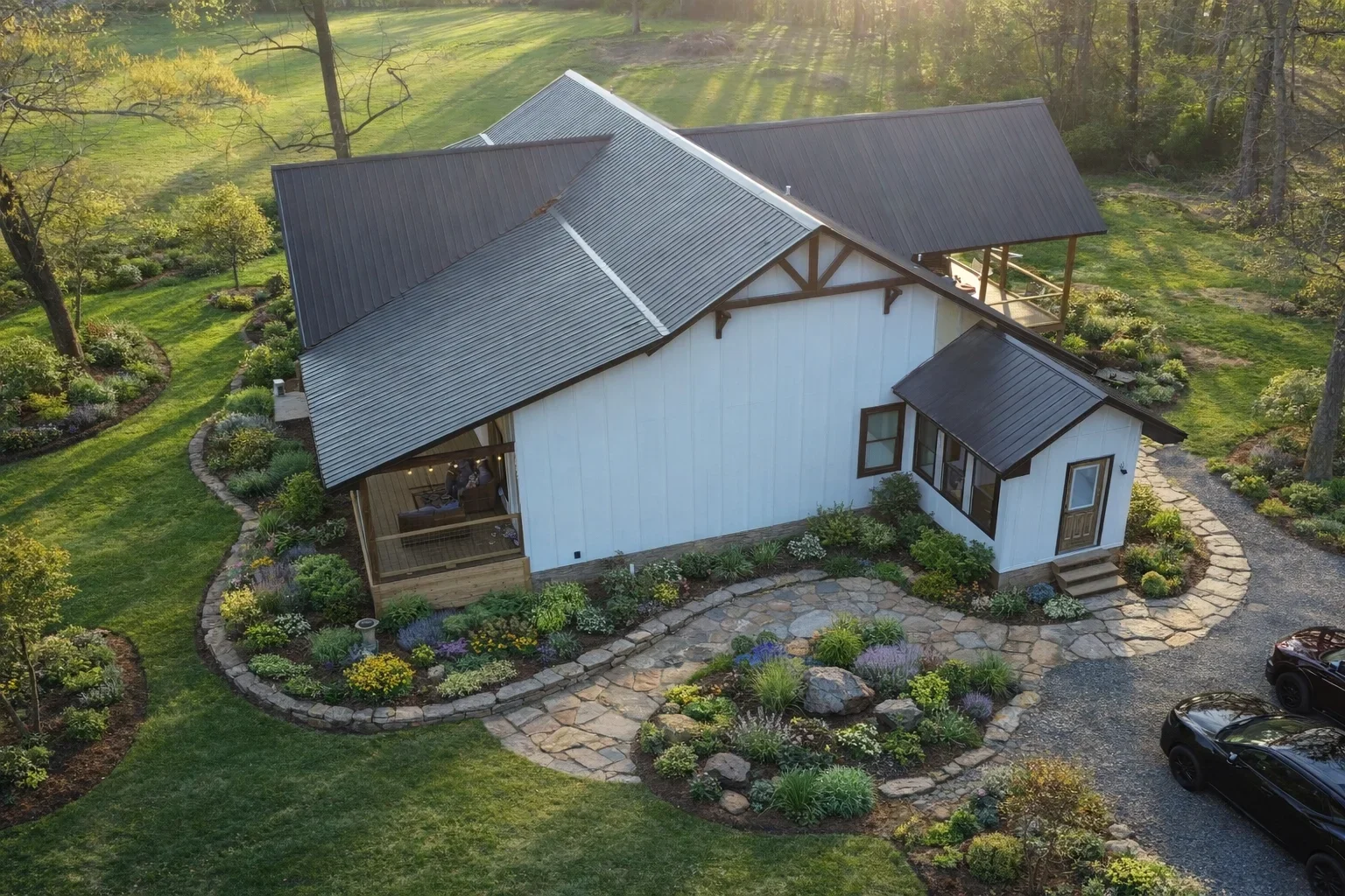 White farmhouse with charcoal metal roof, stone patio, and landscaped grounds