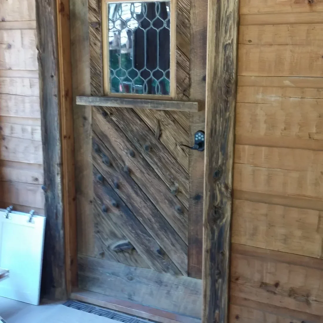 Rustic wood entry door with diagonal grain pattern and geometric glass panel in log cabin exterior